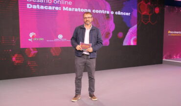 Imagem Do Diretor Executivo Da Abrale, Fábio Fedozzi, A Frente Do Telão Sobre A Competição Realizada No 7º Congresso Todos Juntos Contra O Câncer