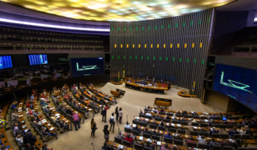 imagem interna da câmara dos deputados brasileira, cadeiras estão dispostas em direção à mesa principal