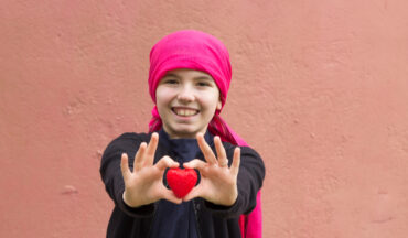 imagem de uma criança com um laço na cabeça, sorrindo e segurando um objeto em formato de coração