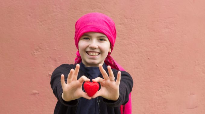 Imagem De Uma Criança Com Um Laço Na Cabeça, Sorrindo E Segurando Um Objeto Em Formato De Coração