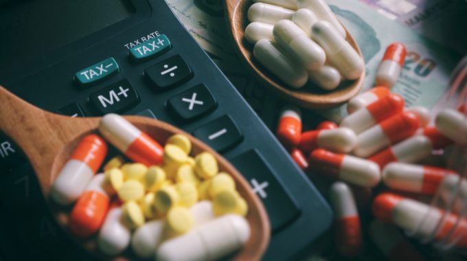 Imagem De Pílulas Medicativas Em Uma Superfície Plana, Alguns Aglomeradas Em Duas Colheres De Madeira Que Estão Próximas à Uma Calculadora Em Representação à Isenção De Impostos Aos Medicamentos Que Tratam O Câncer