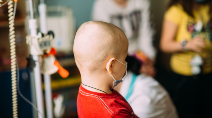 Imagem De Uma Criança, Paciente De Câncer, De Costas Junto De Outras Pessoas Em Uma Sala No Hospital