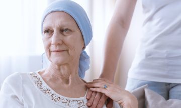Imagem De Uma Mulher Idosa Com Câncer, Apresenta Um Lenço Na Cabeça, E Está Segurando A Mão De Outra Pessoas Que A Conforta