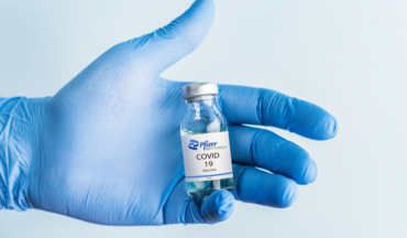 imagem de uma mão com luvas segurando um frasco da vacina da Pfizer