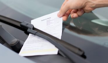 imagem de uma multa em papel sendo colocada no para-brisa de um carro