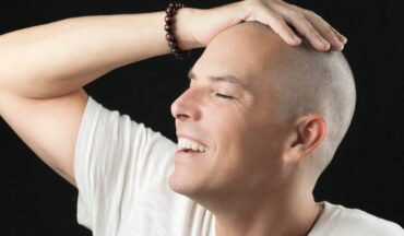 Homem com câncer sorrindo com as mãos na cebeça