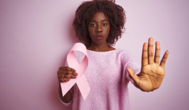 imagem de uma mulher negra segurando o laço da campanha Outubro Rosa e a outra mão aberta e estendida à frente