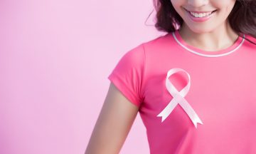 Imagem De Uma Mulher Olhando Para O Laço Da Cor Da Campanha Outubro Rosa Que Está Colado Em Sua Camiseta Próximo Ao Peito
