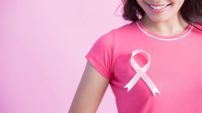 Imagem De Uma Mulher Olhando Para O Laço Da Cor Da Campanha Outubro Rosa Que Está Colado Em Sua Camiseta Próximo Ao Peito