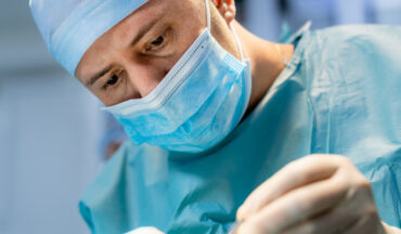 Imagem De Um Profissional Da Saúde Com Máscara, E Luvas Realizando Uma Cirurgia