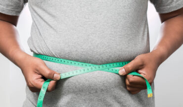 imagem de um homem com sobrepeso segurando um fita métrica ao redor da barriga